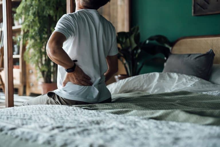 Man sitting on bed rubbing lower back in pain