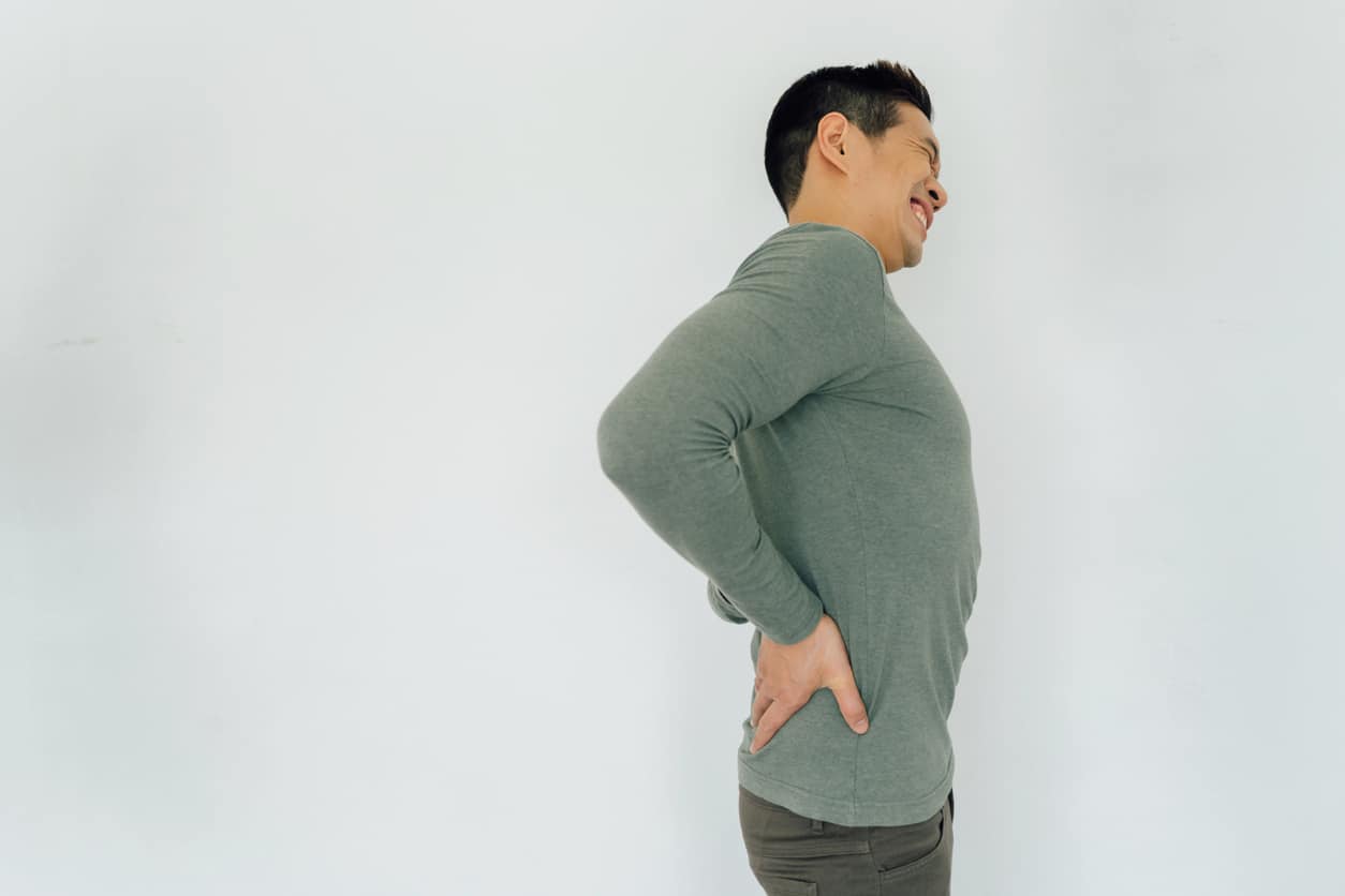 Person placing hands on lumbar area of back and grimacing in pain