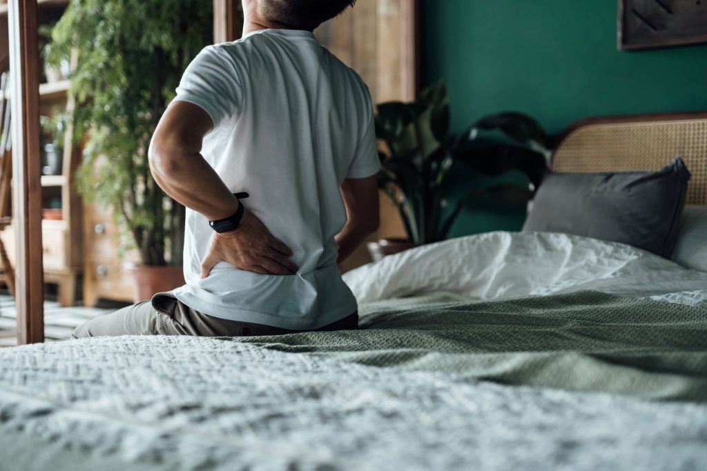 Mature person sitting on bed experiencing lower back pain