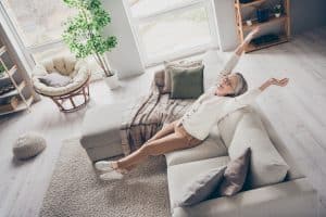 Happy senior person stretching on couch in home living room